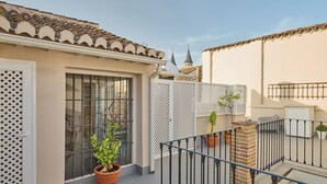 A balcony with potted plants, a metal railing, and a view of a building with a tiled roof. - Apartamentos Luna Suites Palacio Almagra (Granada)