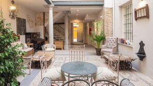 A cozy indoor patio with wicker furniture, a glass table, and a stone wall. - Apartamentos Luna Suites Palacio Almagra (Granada)