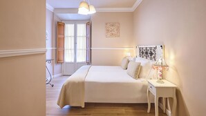 A bedroom with a bed, bedside table, lamp, and a window with curtains. - Apartamentos Luna Suites Palacio Almagra (Granada)