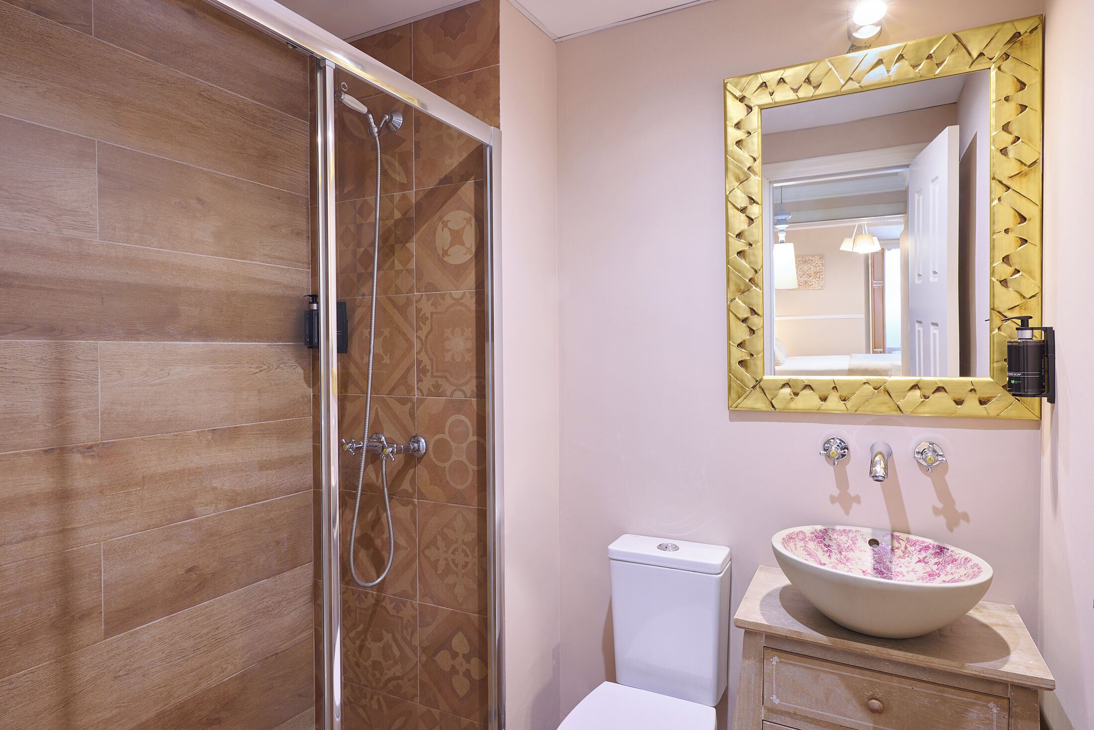 A bathroom with a glass shower enclosure, a toilet, a sink with a decorative basin, and a mirror with a geometric frame.