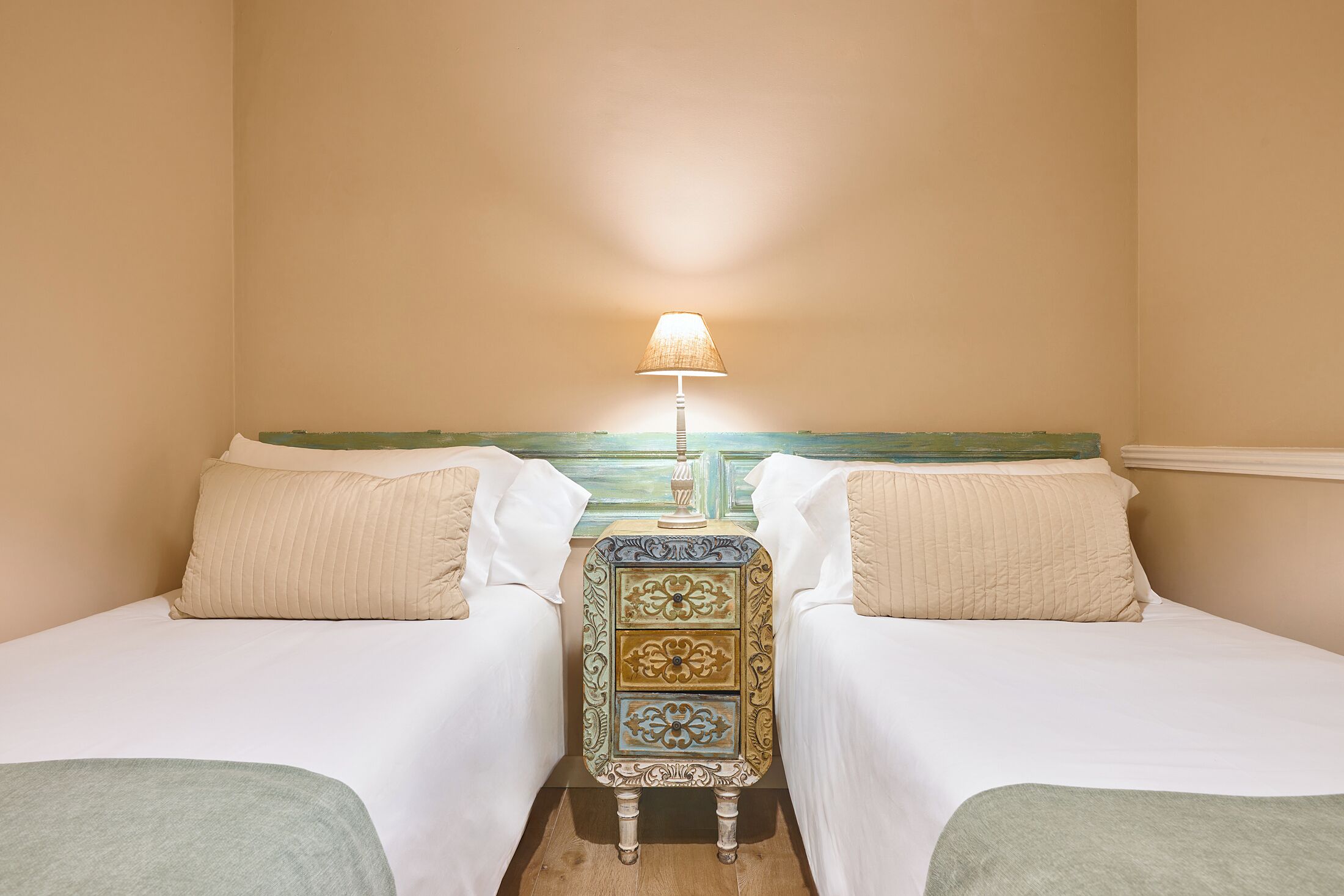 A room with two beds, a nightstand with a lamp, and a decorative cabinet.