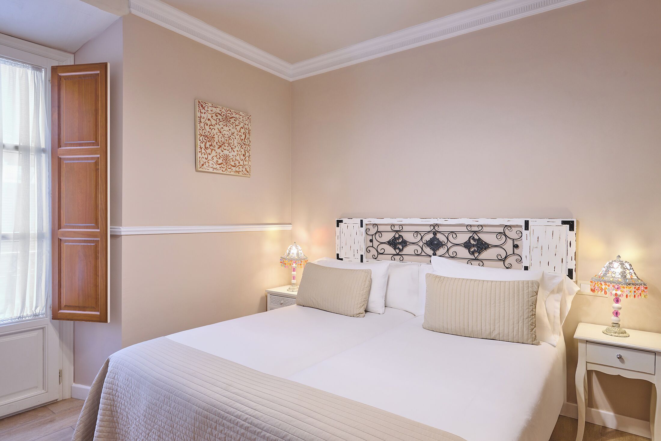 Un dormitorio ordenado con cama, lámparas de noche, un cabecero decorativo y una ventana con cortinas.