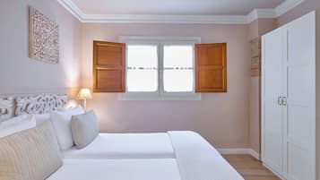 A bedroom with a bed, a nightstand, a lamp, a window with shutters, and a wardrobe.