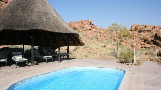 Zona de piscina con sillones de descanso y una estructura de techo de paja.