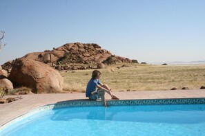 Une personne assise au bord d’une piscine, avec un paysage rocheux en arrière-plan.