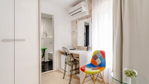 A modern room with a white desk, a colorful chair, a glass table with a vase, and an air conditioning unit. - Palace Tartaglia (Split)