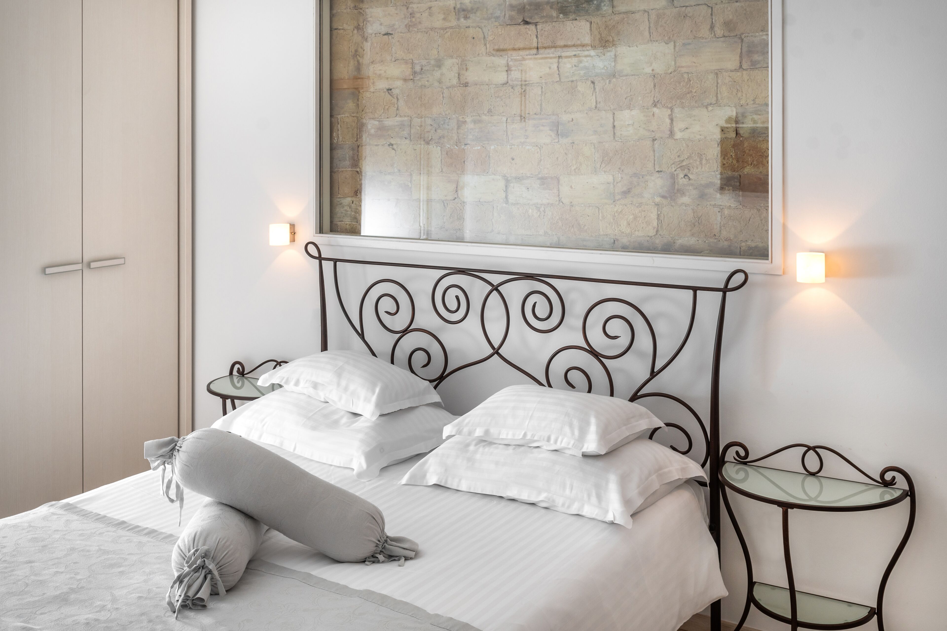 Cama bem arrumada com lençóis brancos, cabeceira de metal e duas mesas de cabeceira com abajures.