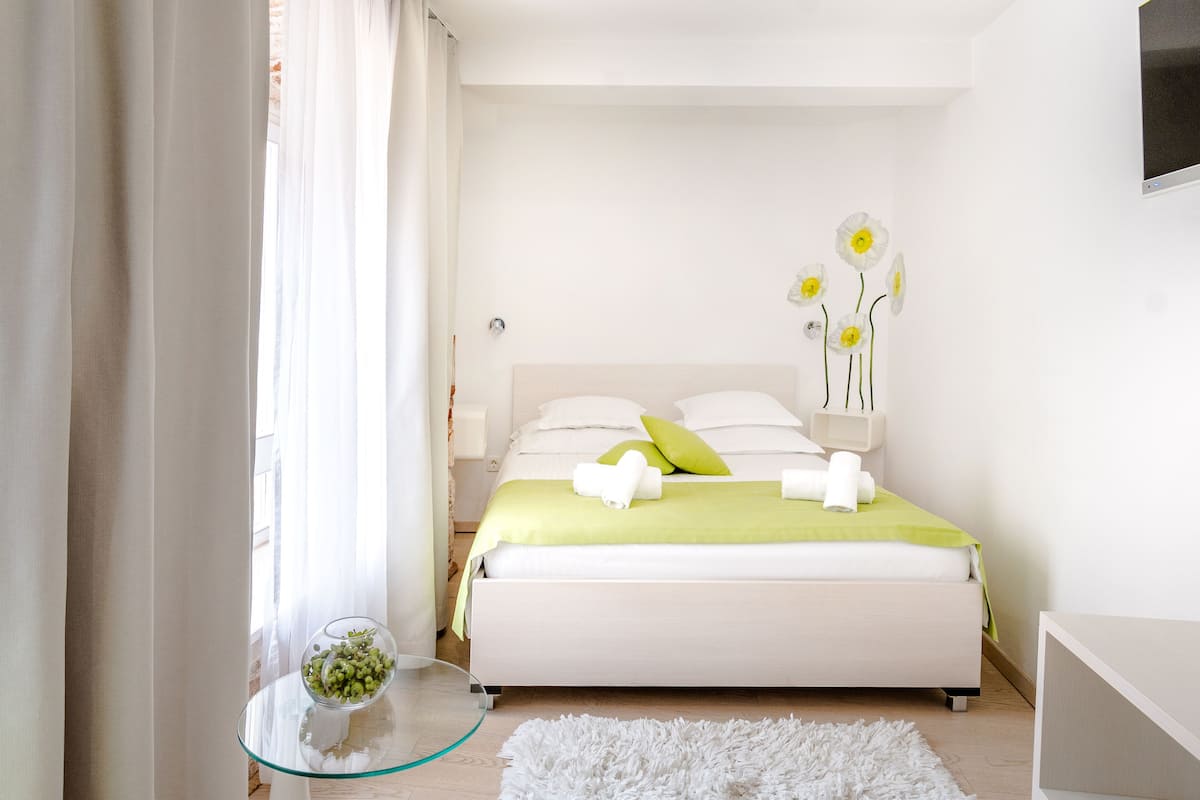 Un dormitorio con una cama, una mesita de vidrio con un cuenco de flores y una alfombra blanca.