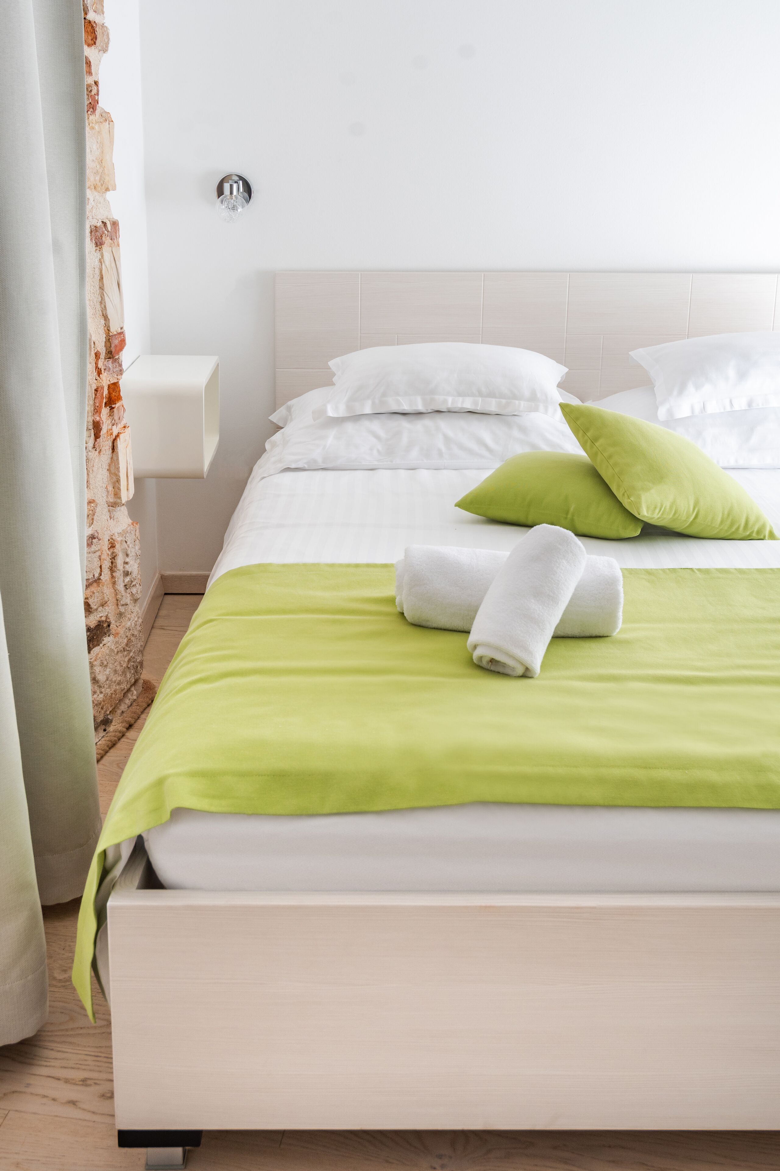 A neatly made bed with white and green bedding, a bedside table, and a wall-mounted light fixture.