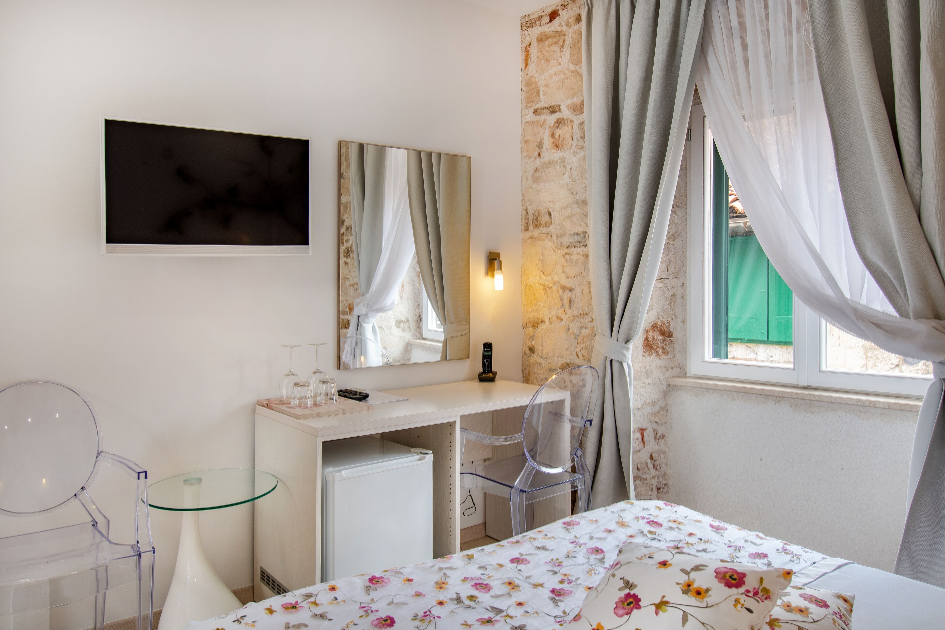 Ein Schlafzimmer mit Bett, Schreibtisch, Stuhl, Spiegel und einem Fenster mit Vorhängen.