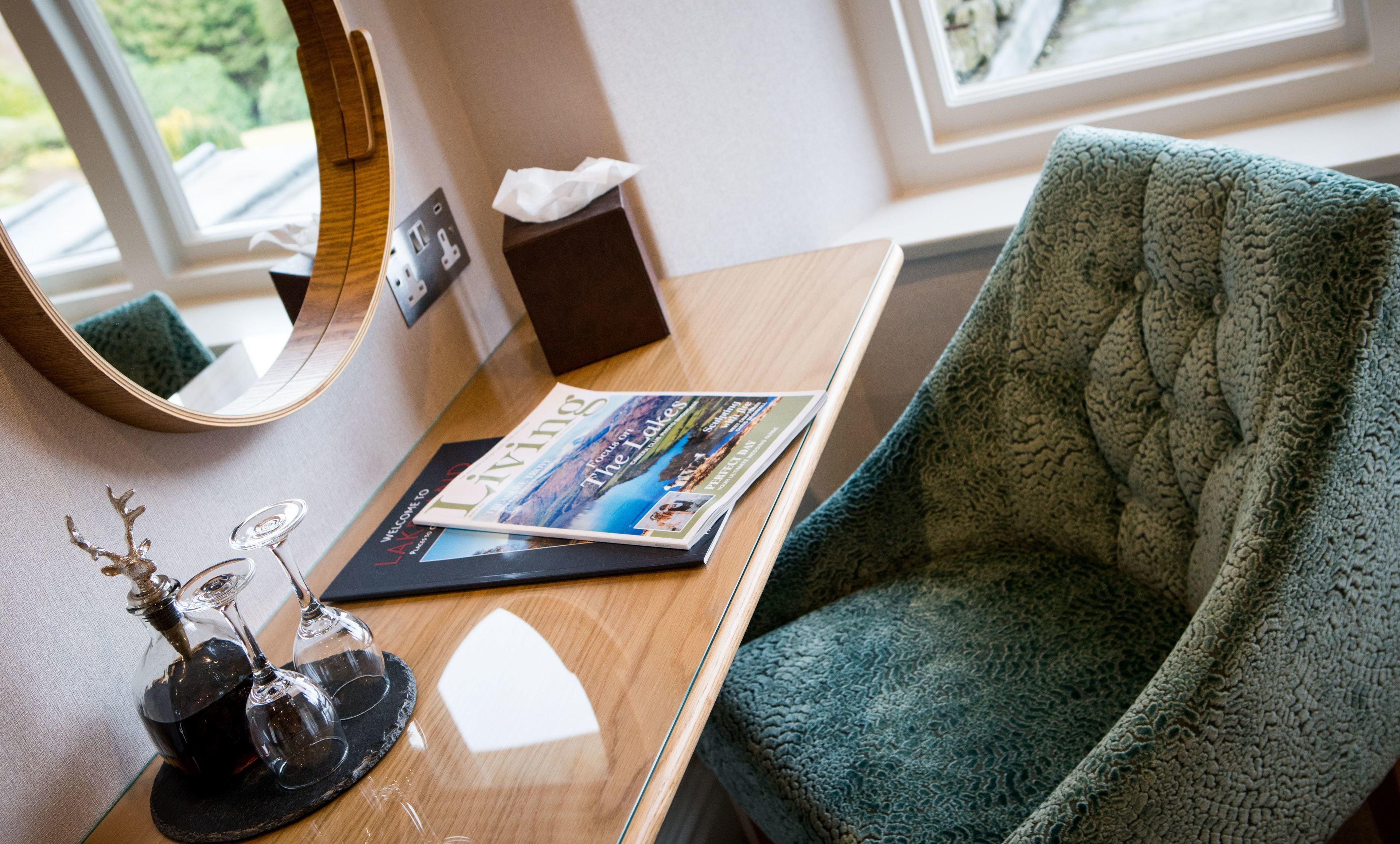 A hotel room with a wooden desk, a magazine, a tissue box, and a green textured chair.
