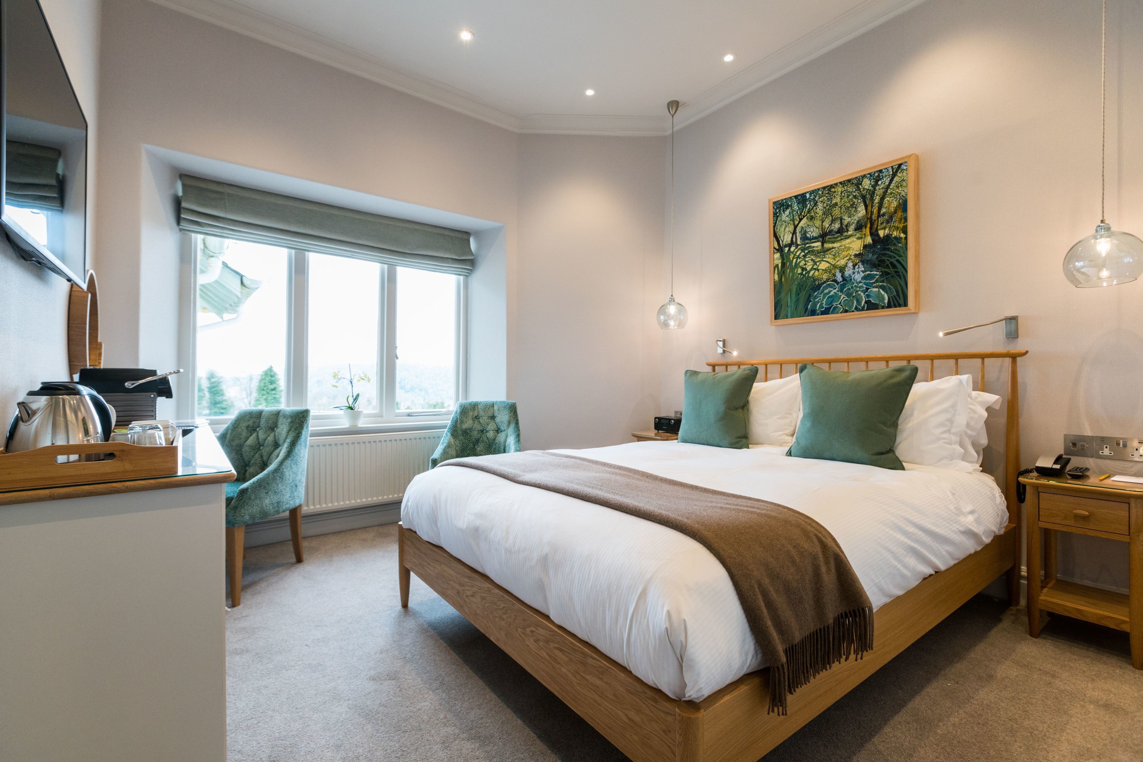 A bedroom with a large bed, a wooden nightstand, a chair, a window with a view, and a painting on the wall.