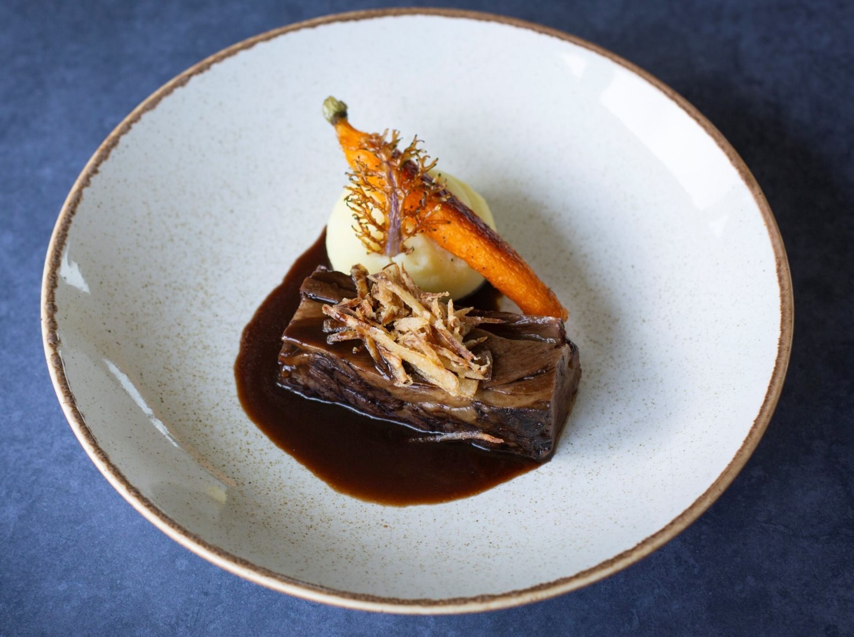 Une assiette contenant un morceau de viande, un légume et une cuillerée de sauce.