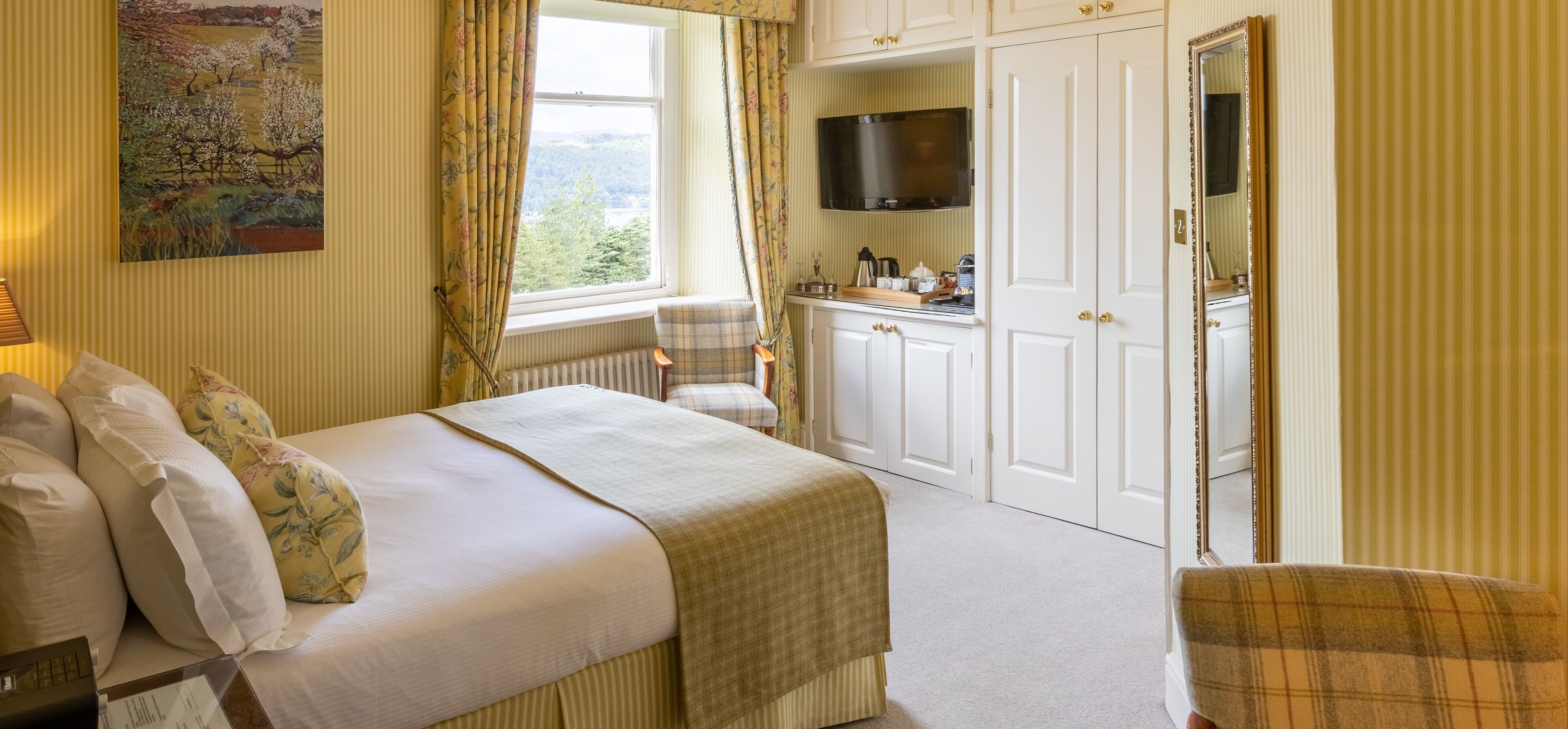 A bedroom with a bed, a chair, a desk, a TV, and a wardrobe.