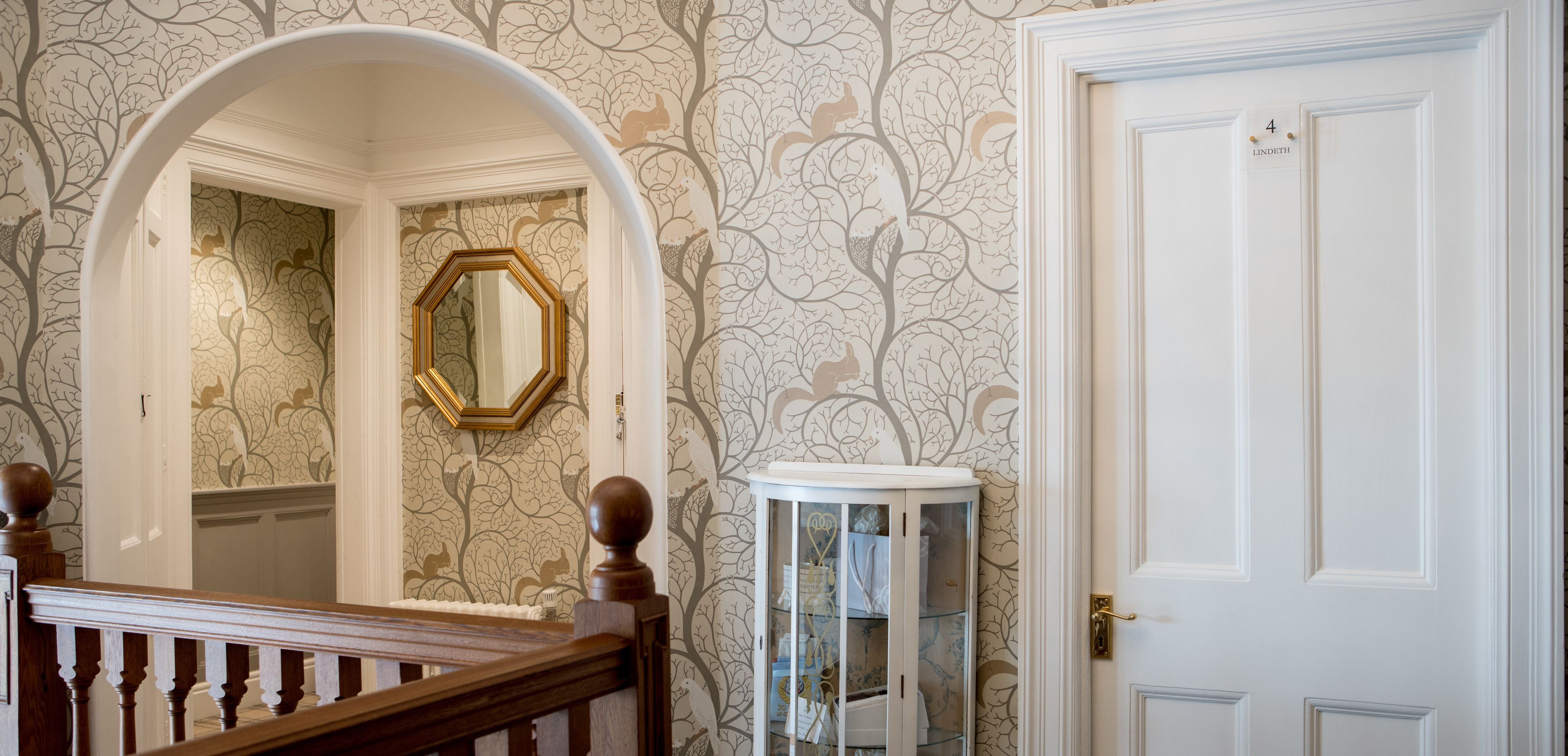 Un couloir avec une porte blanche, un miroir rond et une vitrine.