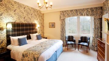 A hotel room with a large bed, two chairs, a dresser, and a window with curtains.