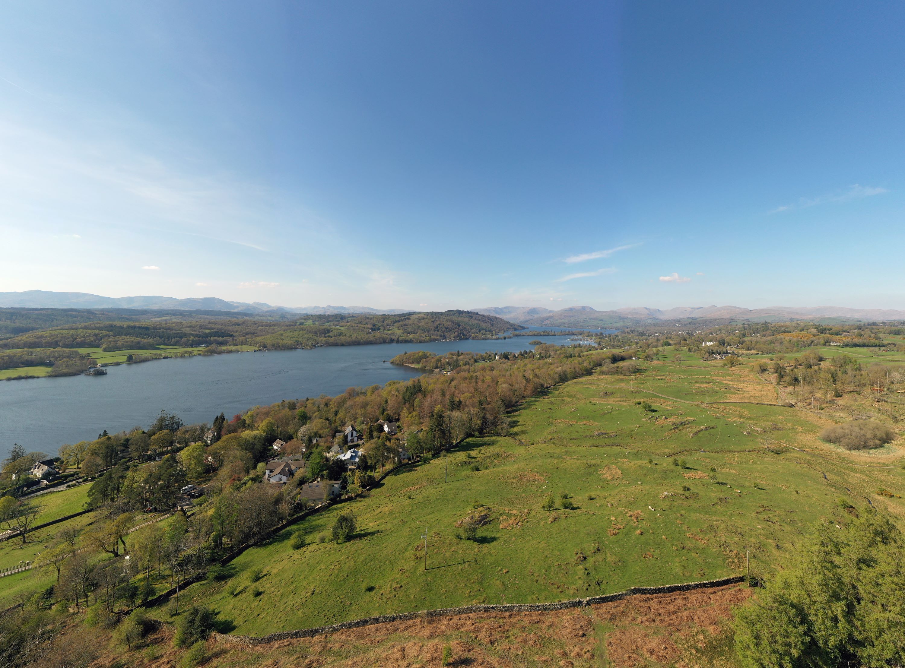 A panoramic view of a lake surrounded by green hills and scattered houses.