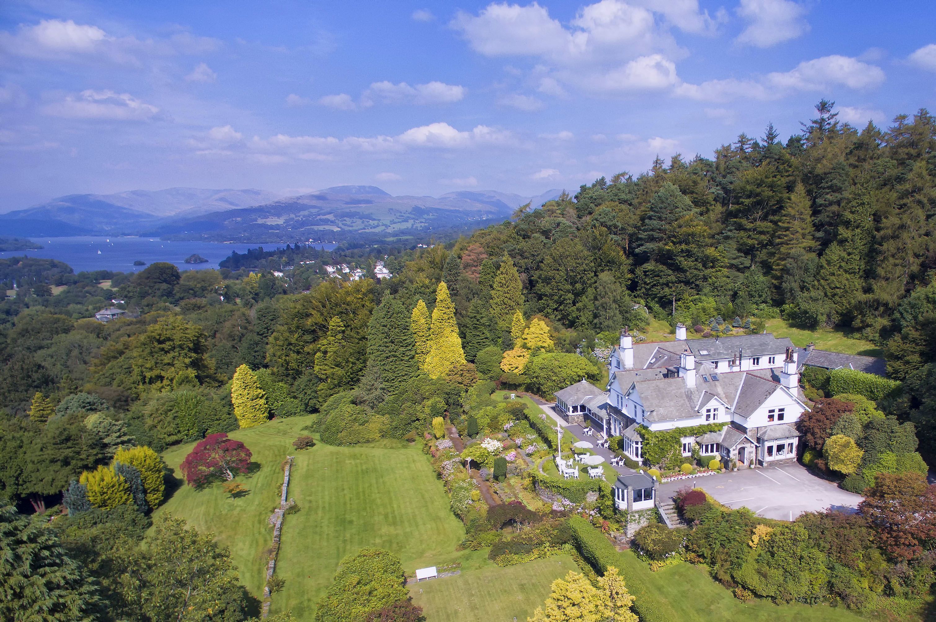 A large, multi-story house surrounded by lush greenery and a lake.