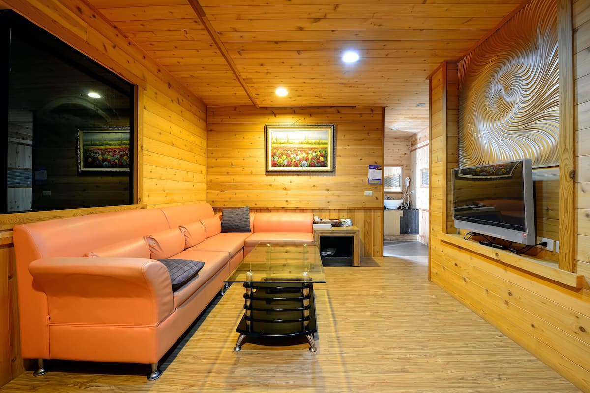A wooden cabin interior with a sofa, glass coffee table, and a TV mounted on the wall.