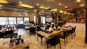 Un restaurante espacioso con varias mesas y sillas, ventanas amplias y una pared de ladrillo.