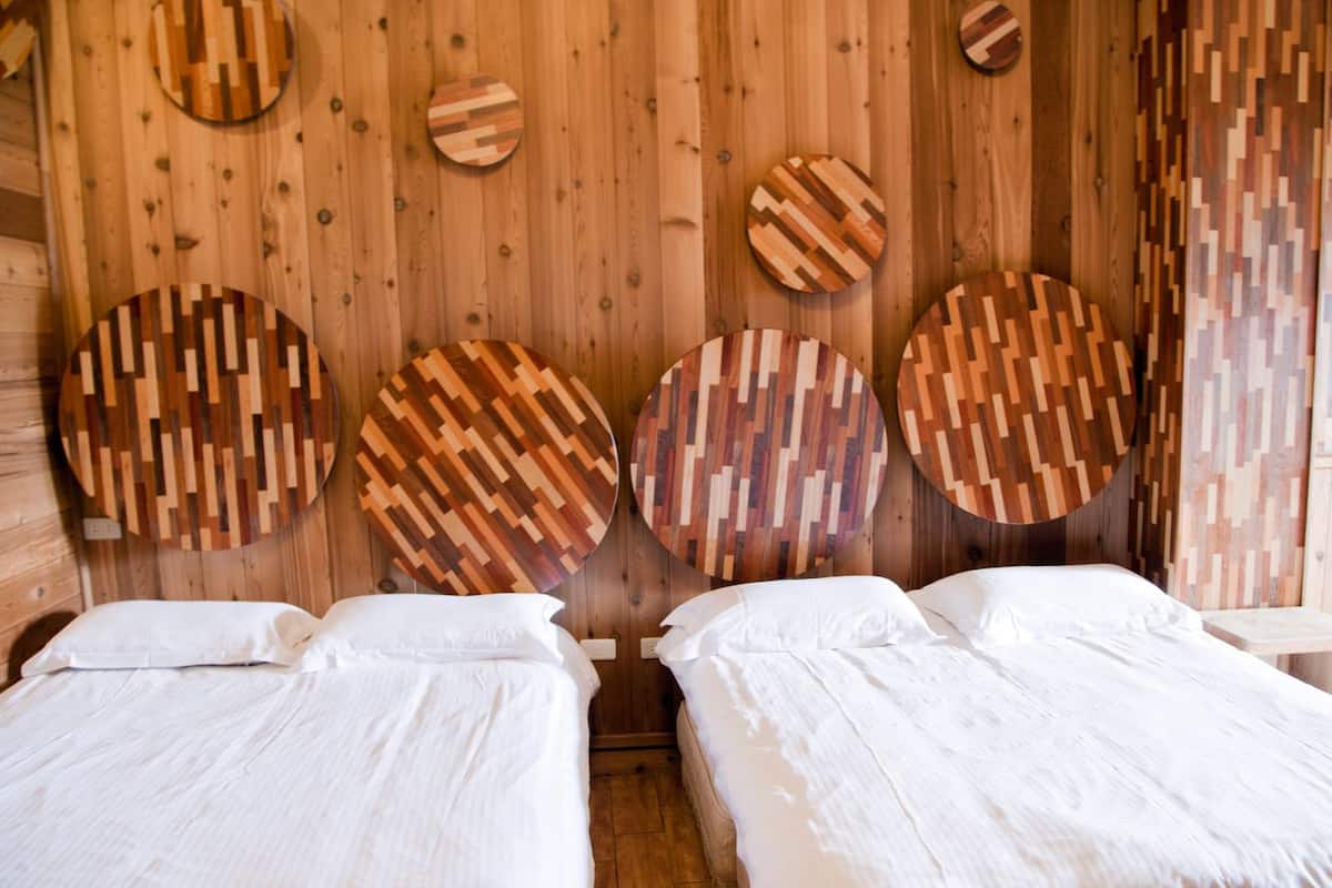 A wooden room with two beds, each with white linens. The walls are adorned with circular wooden panels.