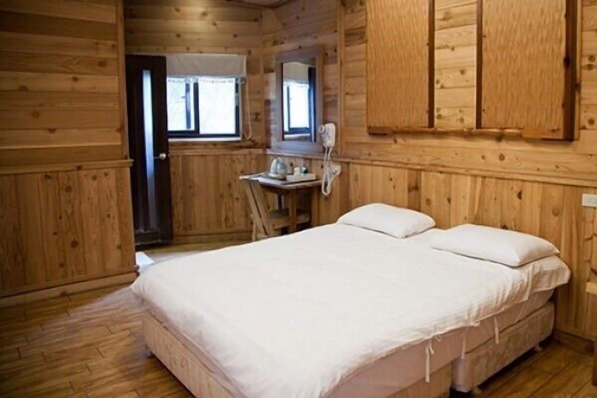 A wooden cabin room with a bed, a small table with a telephone, and a window.