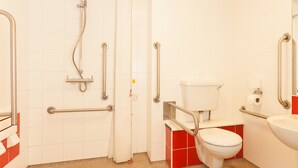 A bathroom with a toilet, sink, and shower. It includes grab bars and a handrail. - Travelodge Cardiff Atlantic Wharf Hotel (Cardiff)