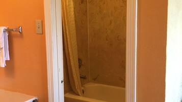 A bathroom with an orange wall, a white bathtub, a white toilet, and a shower curtain.