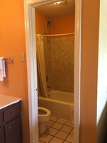 Un baño con pared naranja, una bañera blanca, un inodoro blanco y una cortina de ducha.