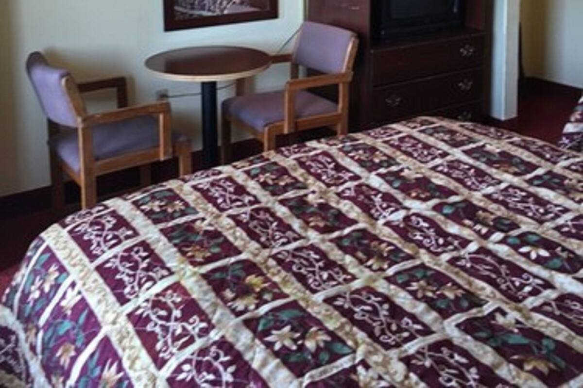 A hotel room with a bed, a TV, a desk with two chairs, and a lamp.