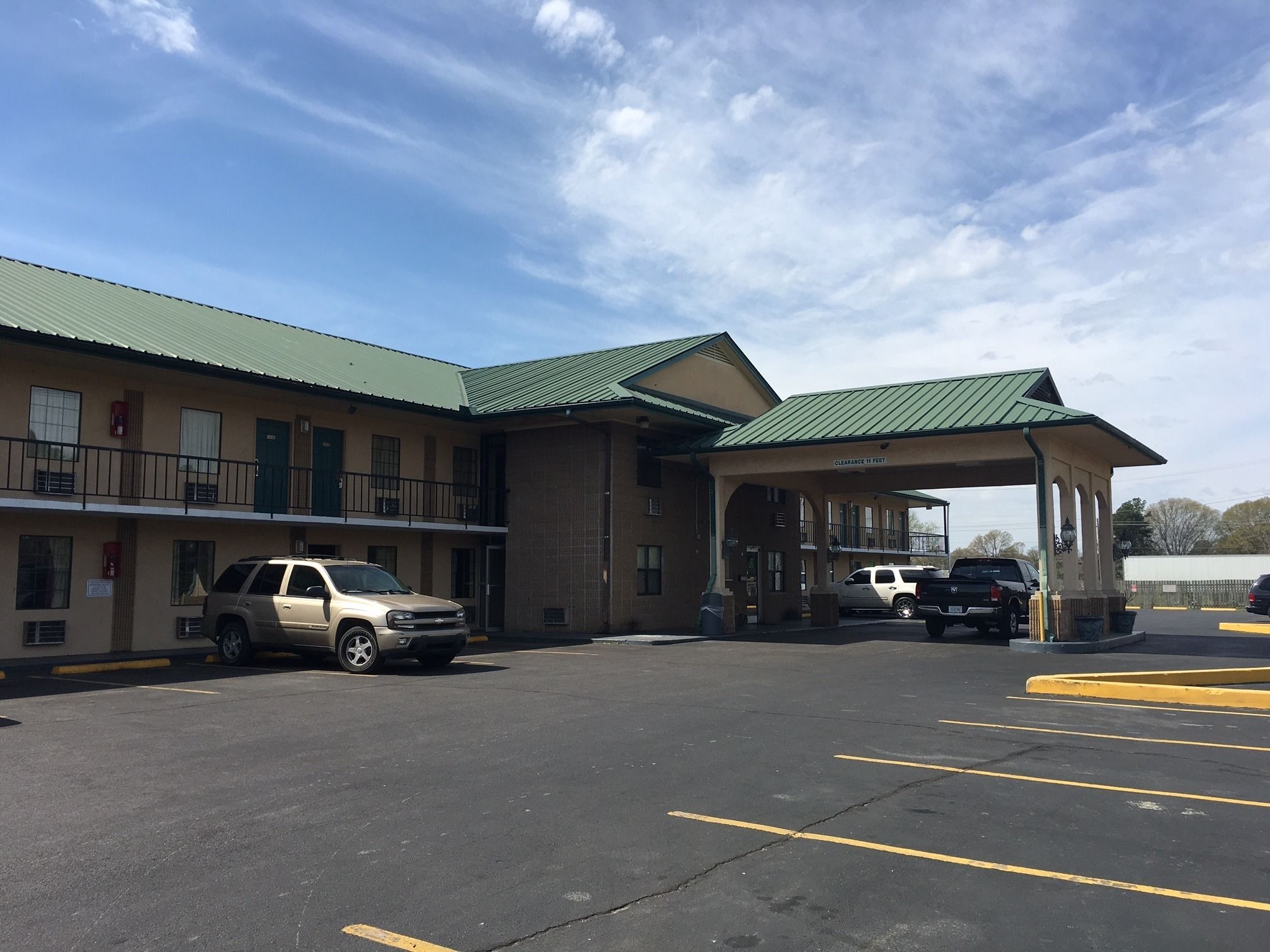 Un motel con techo verde, zona de estacionamiento cubierta y un cartel que indica 'Clearance 11 Feet'.