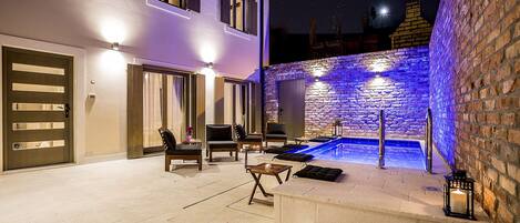 A well-lit outdoor area with a stone wall, a small pool, and seating arrangements.
