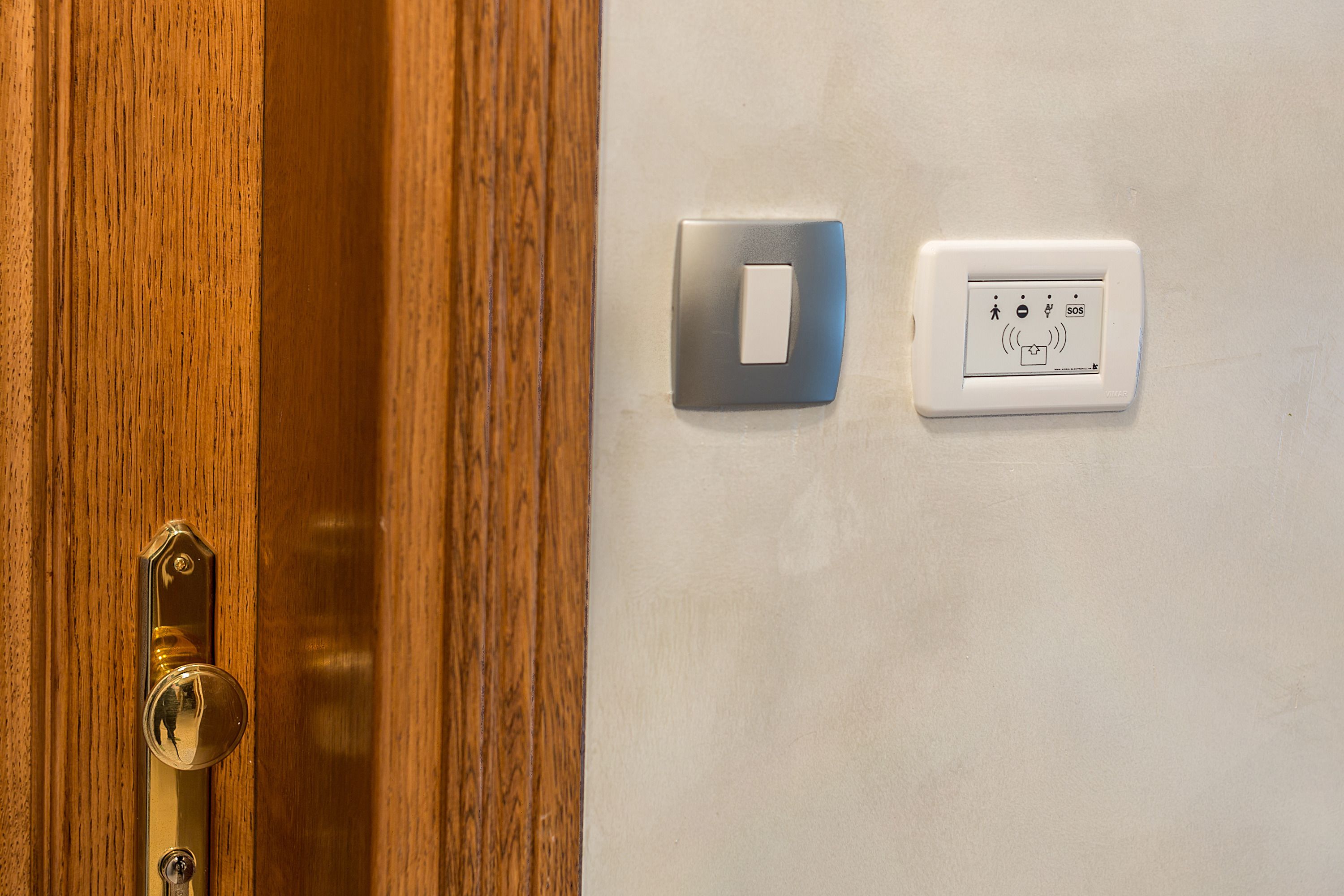 A door with a brass handle and a keyhole, a light switch, and a wall-mounted control panel with icons.
