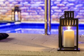 A candle in a black lantern on a stone ledge near a pool with a blurred brick wall in the background.