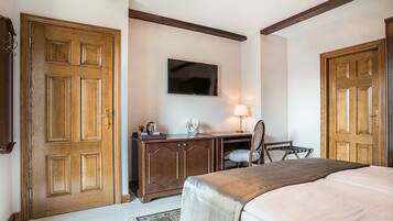 A bedroom with a bed, a desk, a chair, a television, and two wooden doors.