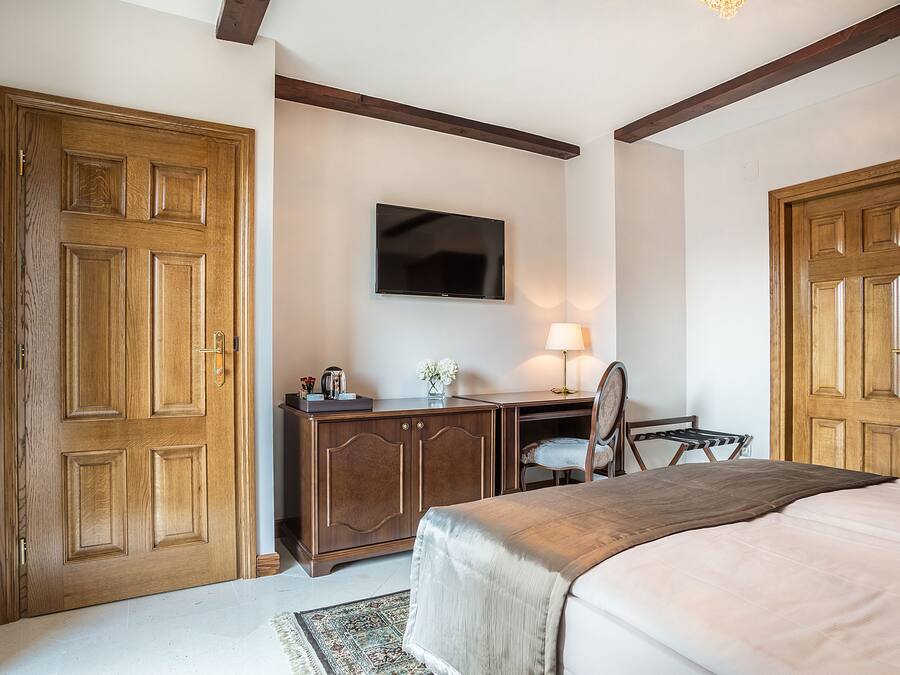A bedroom with a bed, a desk, a chair, a television, and two wooden doors.