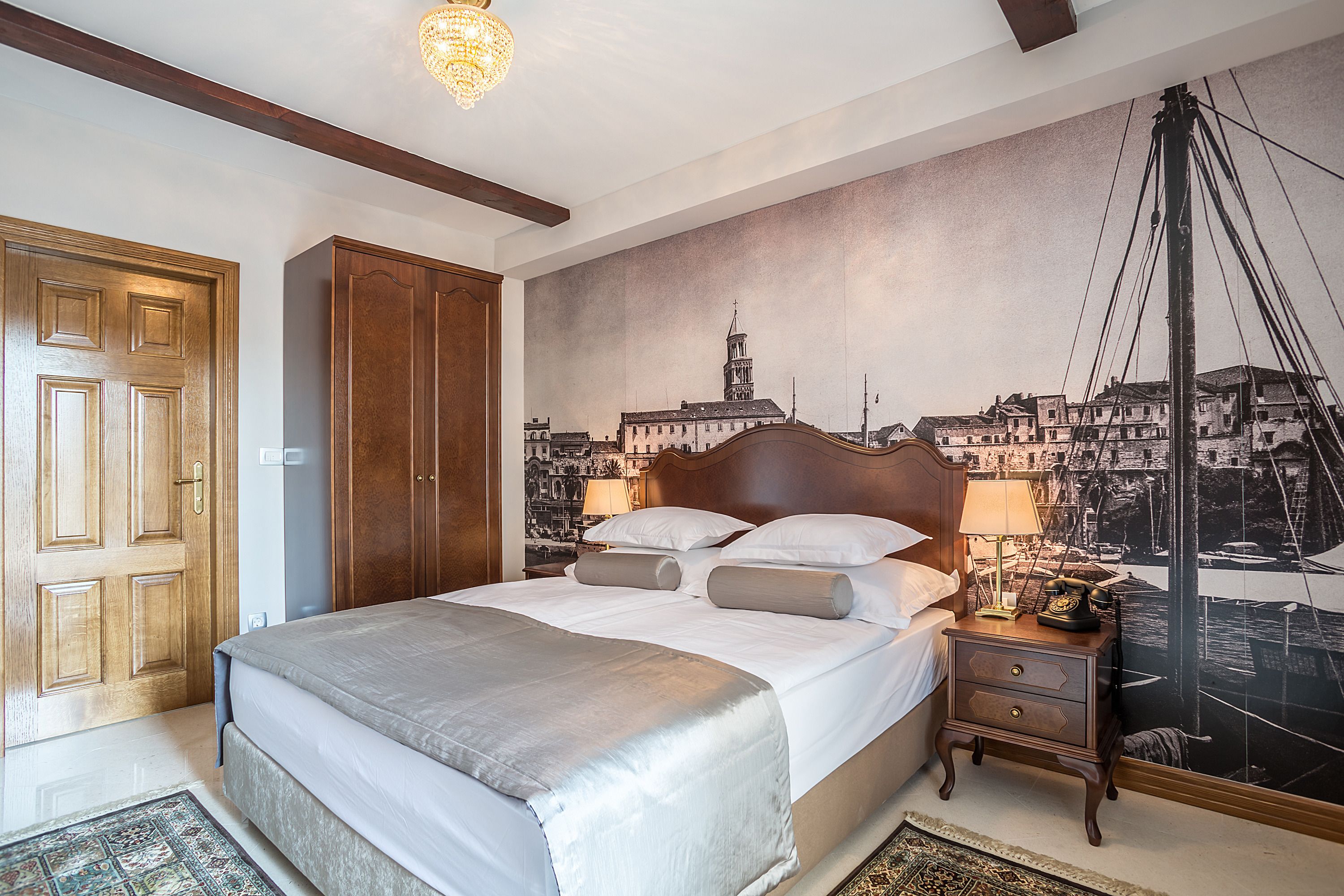 A hotel room with a large bed, wooden wardrobe, and a cityscape mural on the wall.