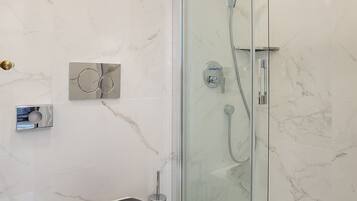A bathroom with a glass-enclosed shower, a toilet, and a marble-tiled wall.