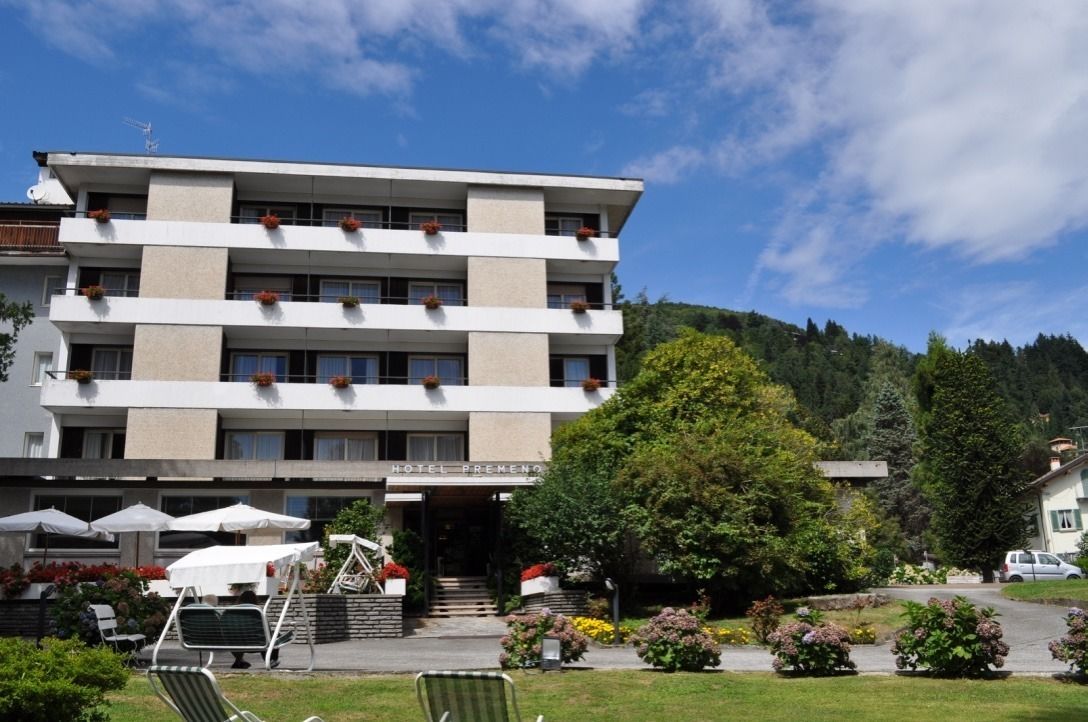 Ein mehrstöckiges Hotel mit schlichter Fassade, einer Außenbereich-Sitzgelegenheit mit Sonnenschirmen und einem Garten mit verschiedenen Pflanzen.