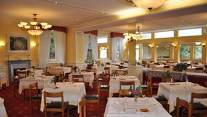 A spacious dining area with multiple tables and chairs, chandeliers, and large windows allowing natural light. - Hotel Premeno (Premeno)