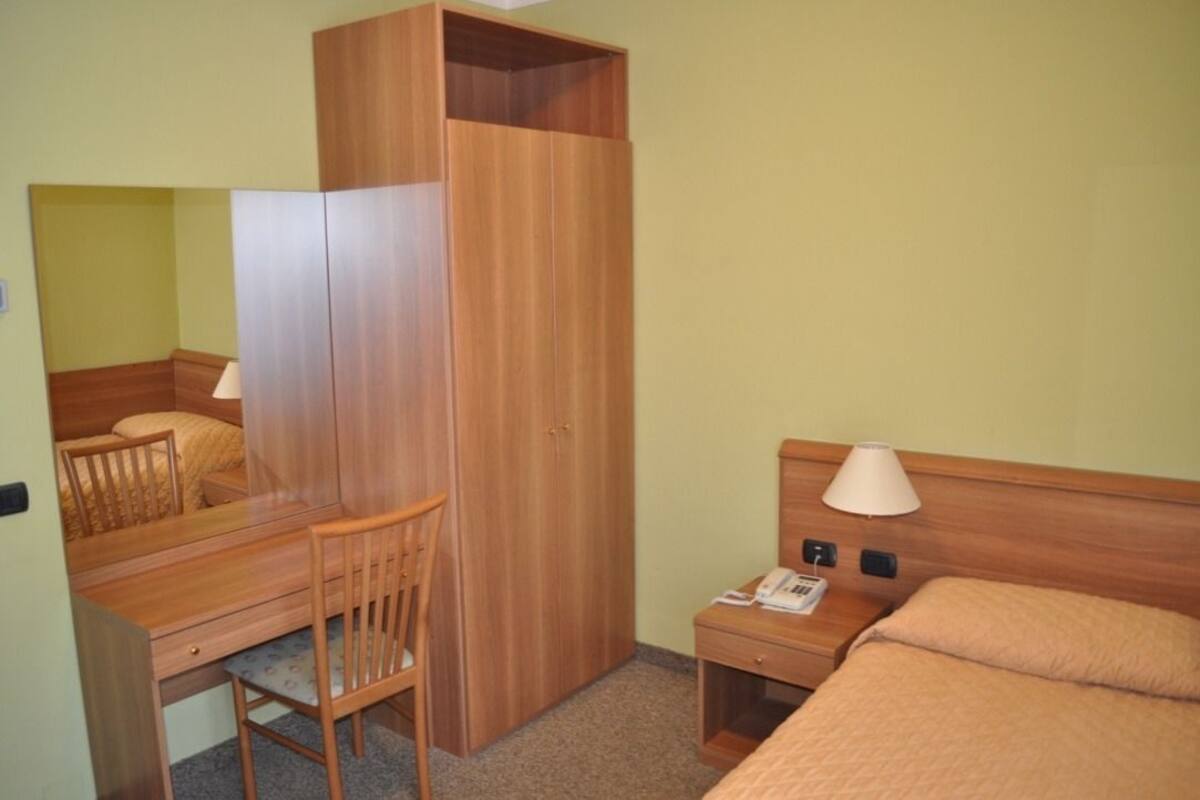 A compact hotel room with a wooden desk, chair, and a bed with a headboard.