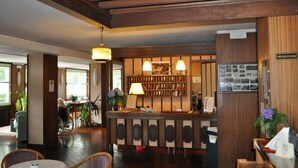 A reception area with a wooden reception desk, a hanging lamp, and a bulletin board with photos. - Hotel Premeno (Premeno)