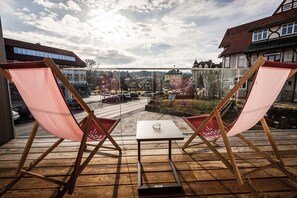 Un balcón con dos sillas plegables rosadas y una mesa pequeña, con vista a una calle con coches y edificios.