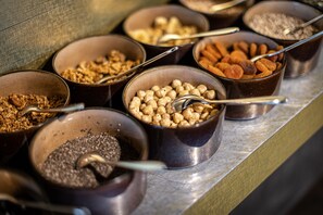 Un bufé con diversos alimentos en cuencos, entre ellos nueces, semillas y granola.