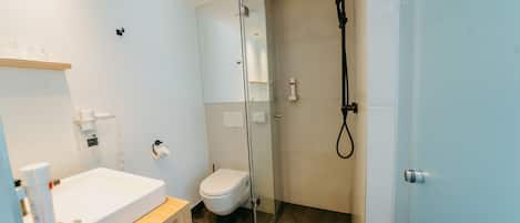 Un baño moderno con ducha de vidrio, lavamanos blanco y retrete.