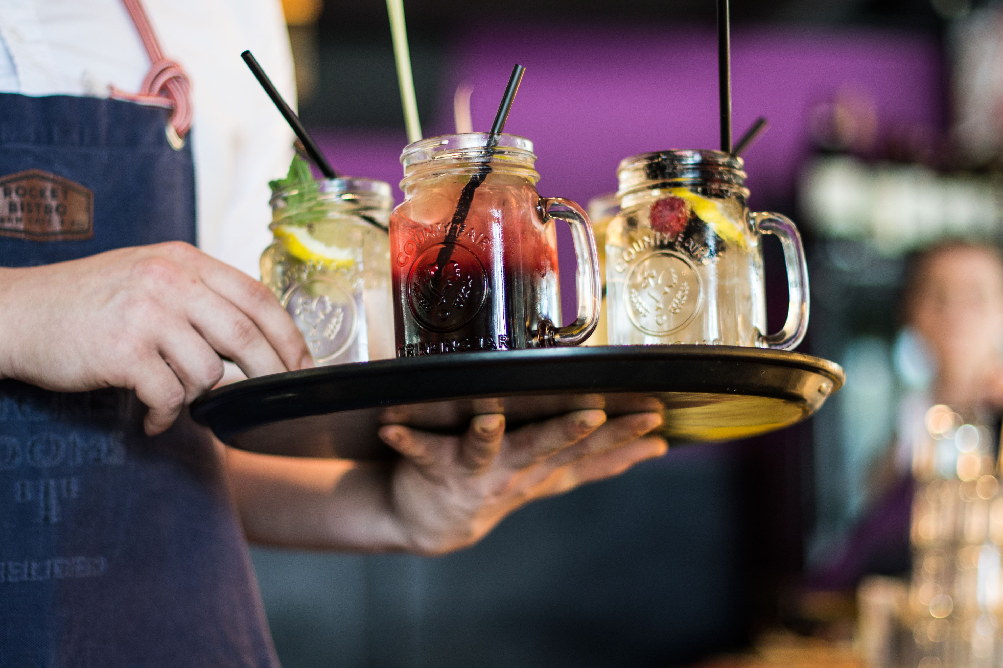 A person holding a tray with three mason jars of beverages.
