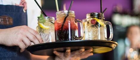 Una persona sostiene una bandeja con tres frascos de vidrio llenos de bebidas.