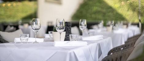 A row of tables with white tablecloths, each set with a wine glass and a water glass.