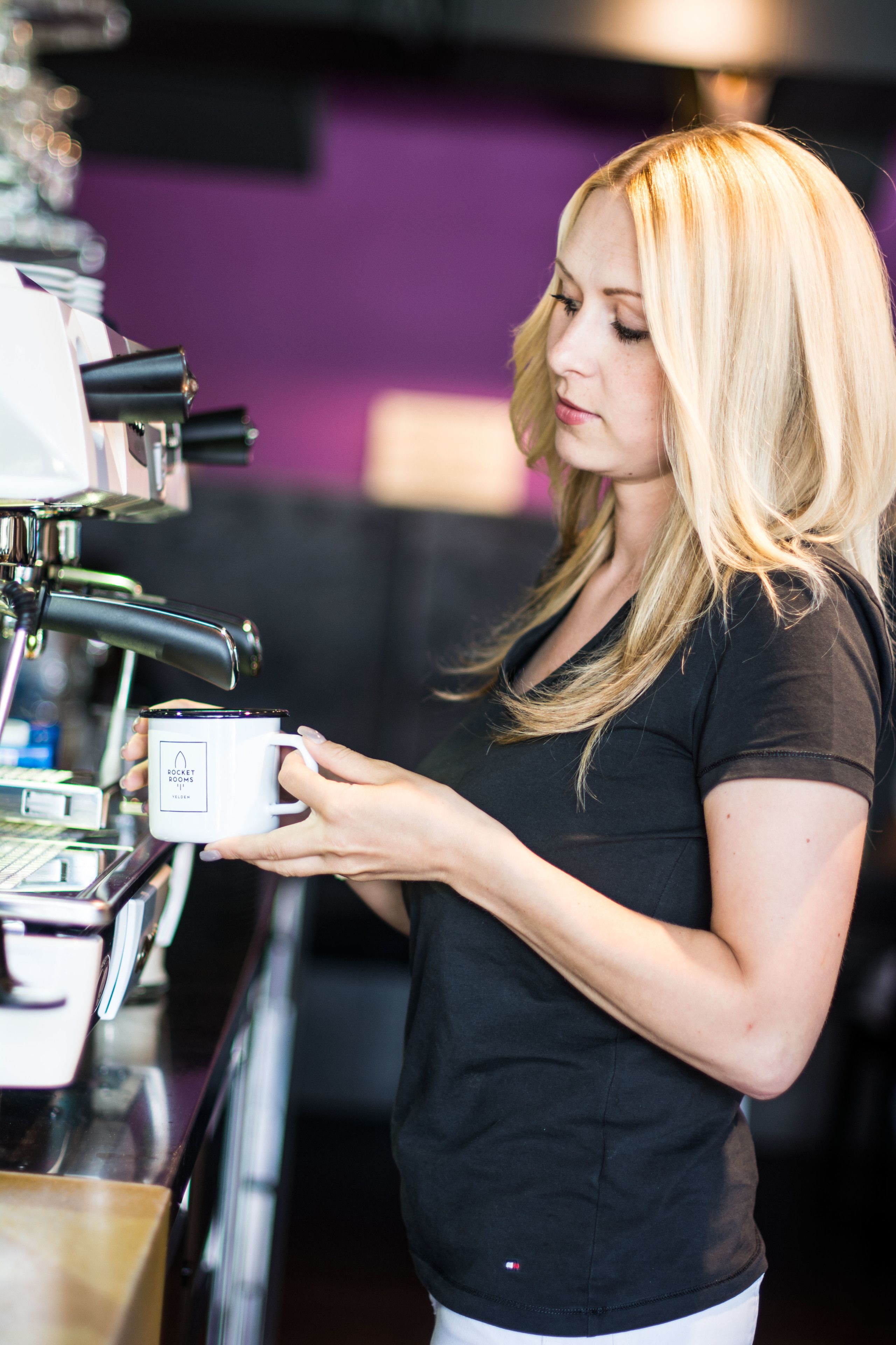 A person holding a mug with a logo, standing in front of a coffee machine.