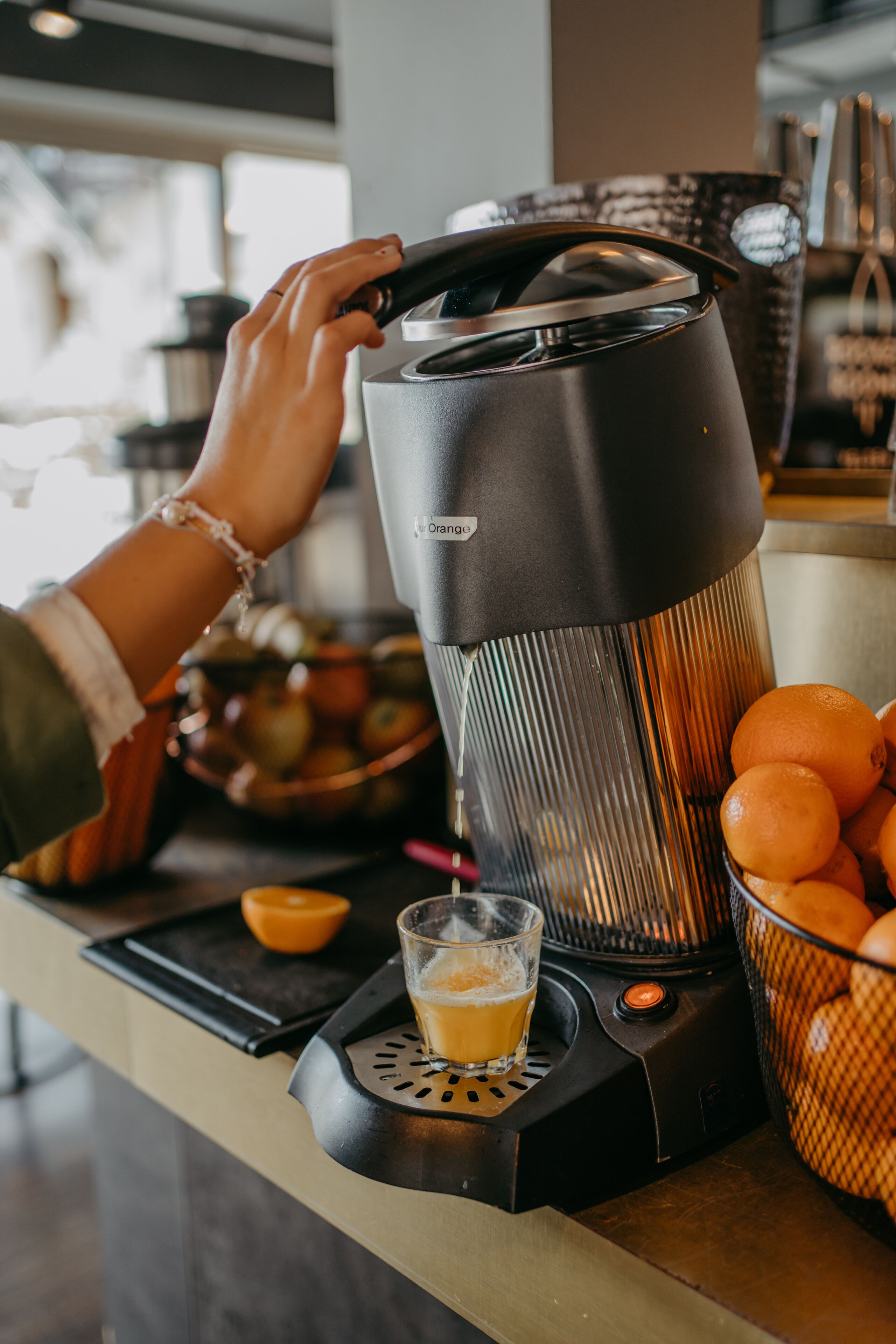 Une machine à café avec une tasse de café posée sur un comptoir, un panier d’oranges et un saladier de pommes.